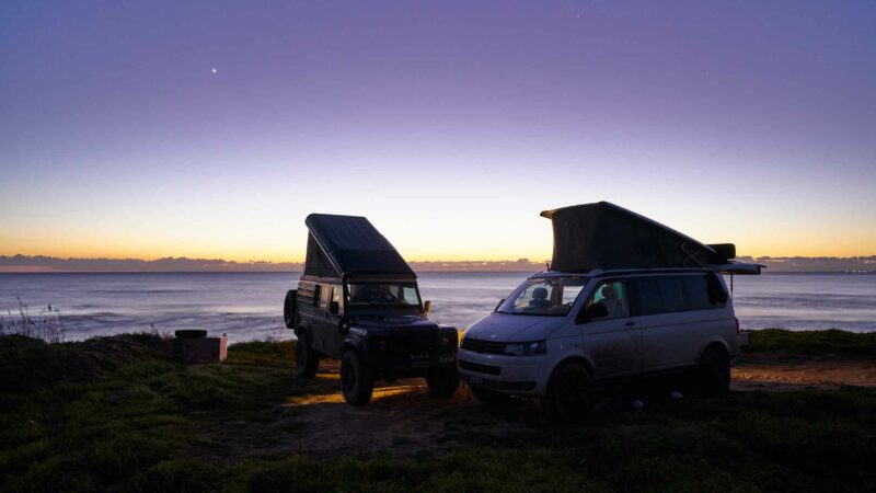 Vanlife-Szene am Meer. Ein Land Rover und ein VW T5 mit Hubdächern am Campieren am Meer.